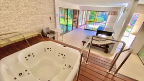 Un baño moderno con una bañera grande, suelo de madera y vistas a un jardín a través de un ventanal.