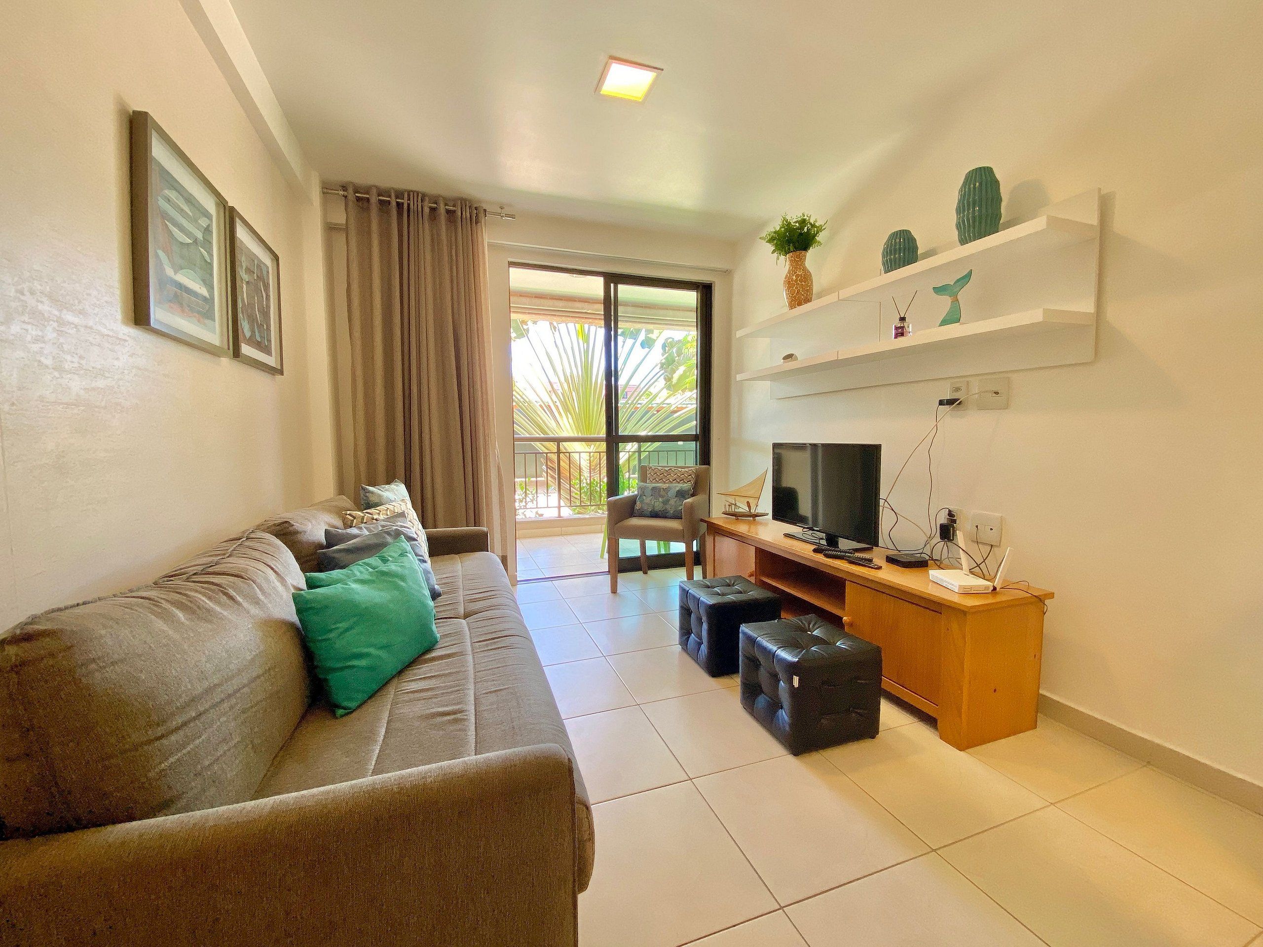 A living room with a sofa, a TV, a desk, and a balcony with a view.