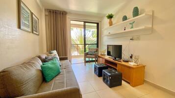 A living room with a sofa, a TV, a desk, and a balcony with a view.