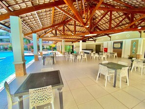 Un patio al aire libre con mesas y sillas, una piscina y una zona de estar cubierta.