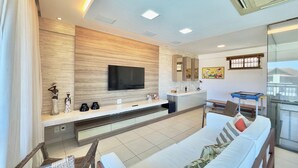 Una habitación de hotel moderna con una televisión de pantalla plana, un sofá, un comedor y un balcón con barandilla de vidrio.