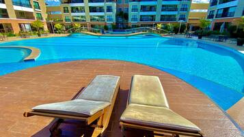 A swimming pool with lounge chairs, a bridge, and a multi-story building with balconies.