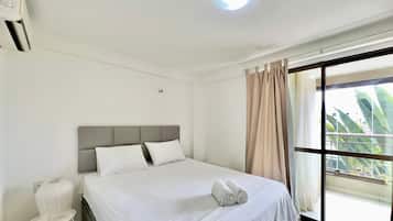 A hotel room with a bed, a bedside table, a lamp, a window with curtains, and a view of greenery outside.