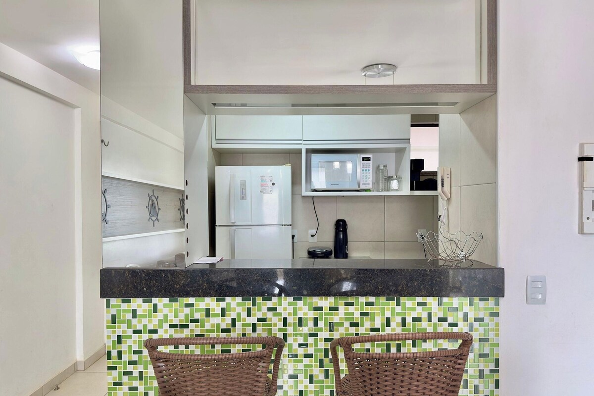 A kitchen with a black countertop, two wicker chairs, a microwave, and a refrigerator.