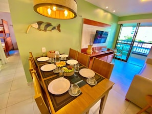 A dining area with a table set for four, a television, and a view of the outdoors. - Condominio Mediterranee Residence por Be My Guest (Aquiraz)