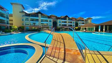 Una piscina de diseño curvo en un resort, rodeada de edificios de varios pisos con balcones.