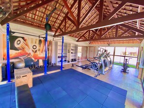 A gym with exercise equipment, a large mirror, and a ceiling with wooden beams. - Condominio Mediterranee Residence por Be My Guest (Aquiraz)