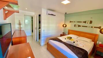 Quarto de hotel com cama, mesa de cabeceira, televisão e escrivaninha de madeira.