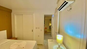 Quarto de hotel com cama, mesa de cabeceira com abajur, telefone e ar condicionado.