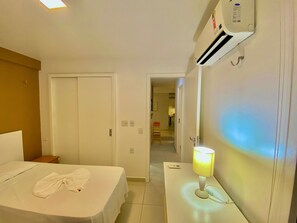 A hotel room with a bed, a bedside table with a lamp, a phone, and an air conditioning unit. - Condominio Mediterranee Residence por Be My Guest (Aquiraz)