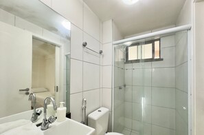 A bathroom with a glass-enclosed shower, a white sink with a mirror, and a toilet. - Condominio Mediterranee Residence por Be My Guest (Aquiraz)