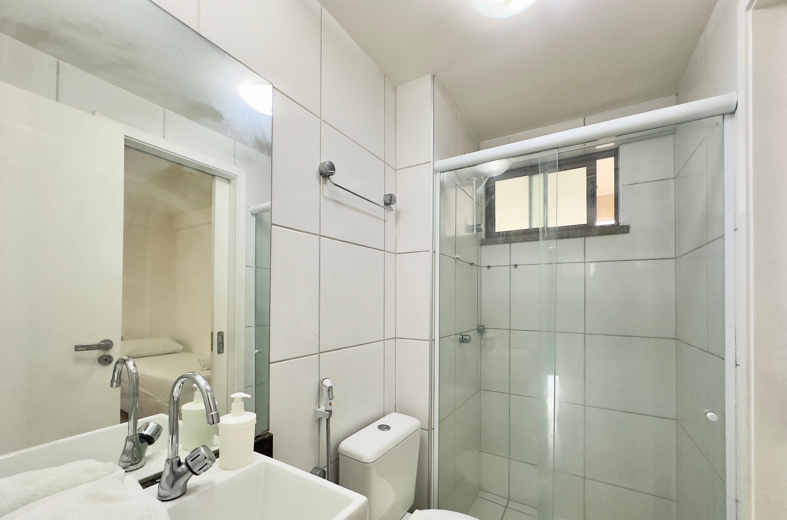 Un baño con ducha envuelta en vidrio, un lavabo blanco con espejo y un inodoro.