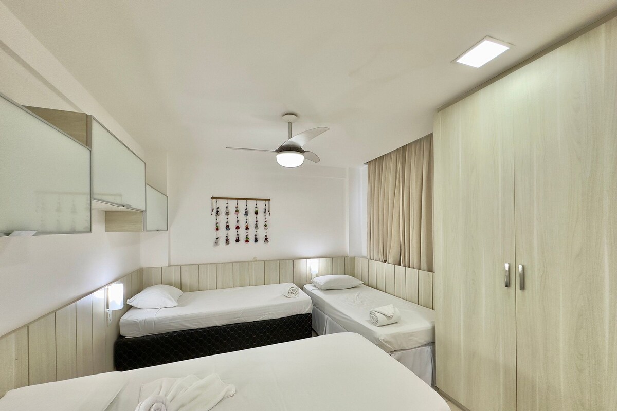 A hotel room with two single beds, a ceiling fan, a large wardrobe, and a wall-mounted mirror.