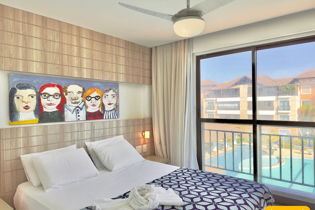 Habitación de hotel con cama, ventilador de techo, ventana grande con vista a la piscina y un cuadro en la pared.
