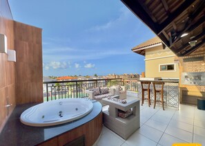 Un balcón con jacuzzi, mobiliario de mimbre y una zona de cocina.