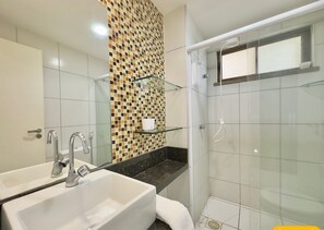 A bathroom with a white sink, a glass shower enclosure, and a tiled wall with a mosaic pattern. - Condominio Mediterranee Residence por Be My Guest (Aquiraz)