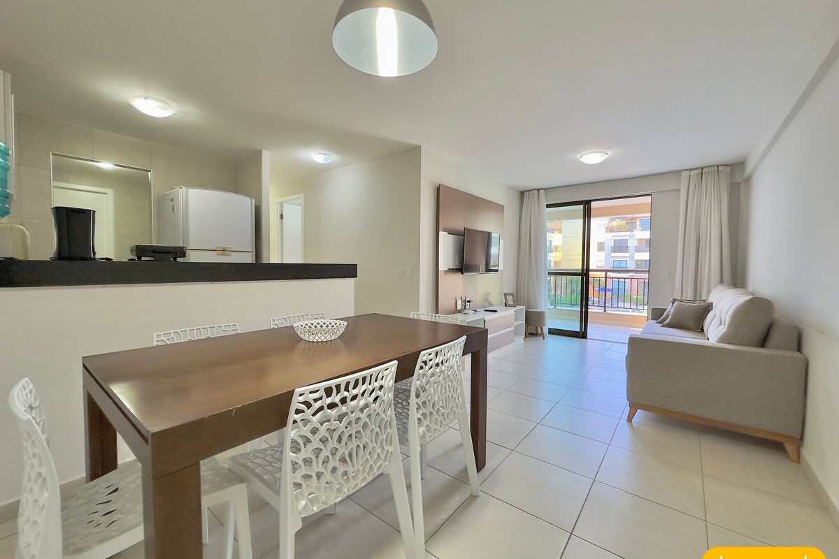 A modern living room with a dining area, a sofa, a TV, and a balcony with a view.