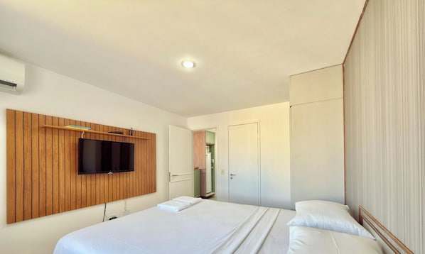 Una habitación de hotel con una cama, un televisor montado en un panel de madera y un armario.