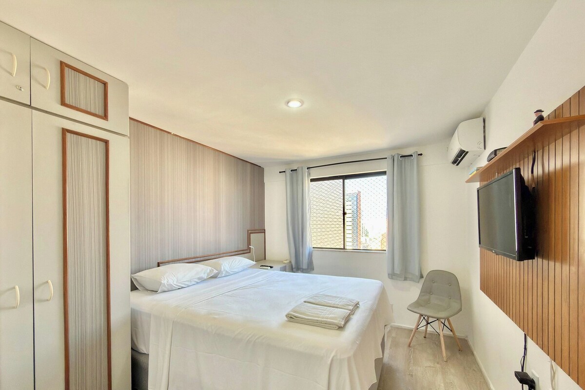 A hotel room with a bed, a chair, a TV, and a window with curtains.