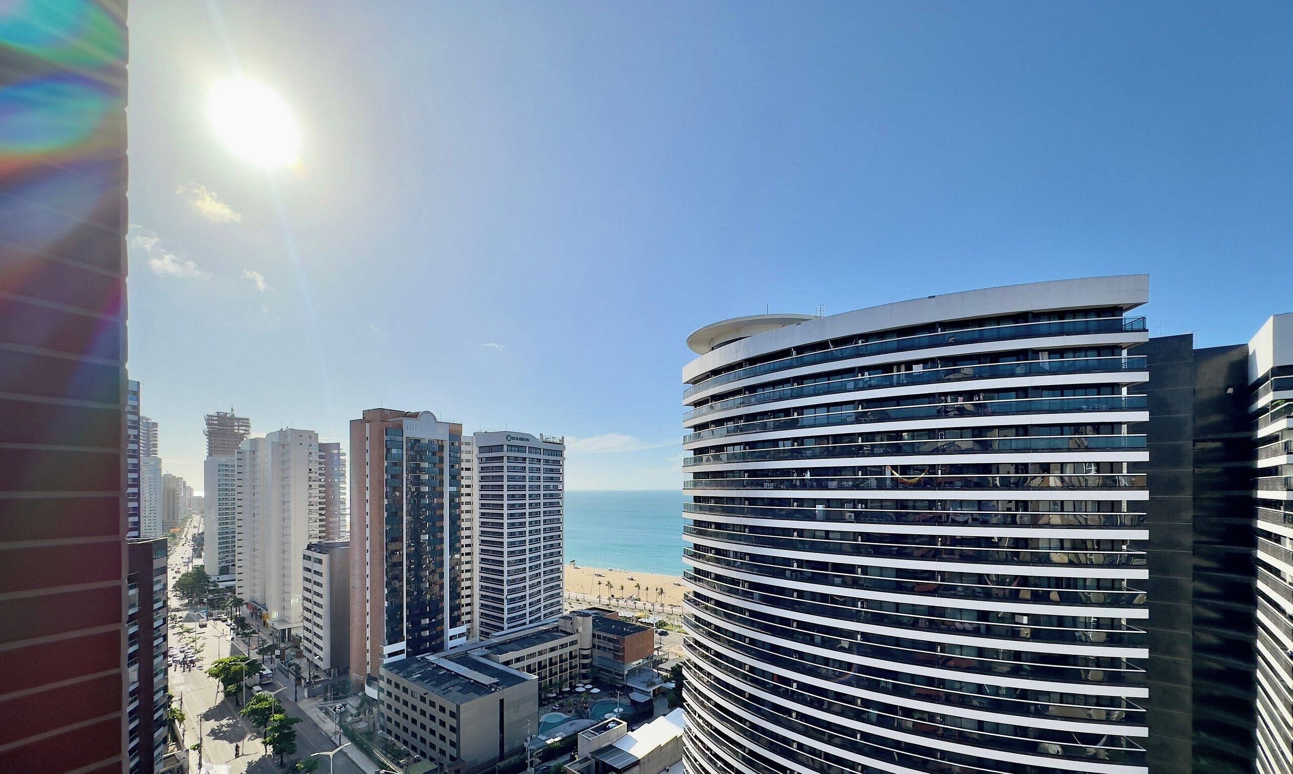 A high-rise building with a curved facade overlooking a beach.