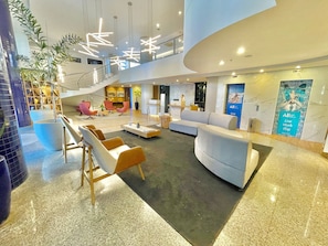 A modern lobby with a curved reception desk, seating areas, and a staircase leading to an upper level.