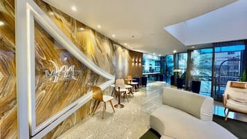 Un moderno vestíbulo de hotel con una pared de mármol, una zona de estar y grandes ventanales.
