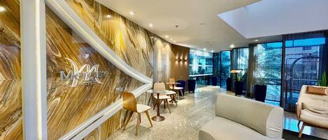 A modern hotel lobby with a marble wall, seating area, and large windows.