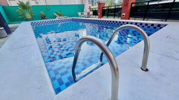 A swimming pool with checkered tiles, metal poolside railings, and a green wall in the background.