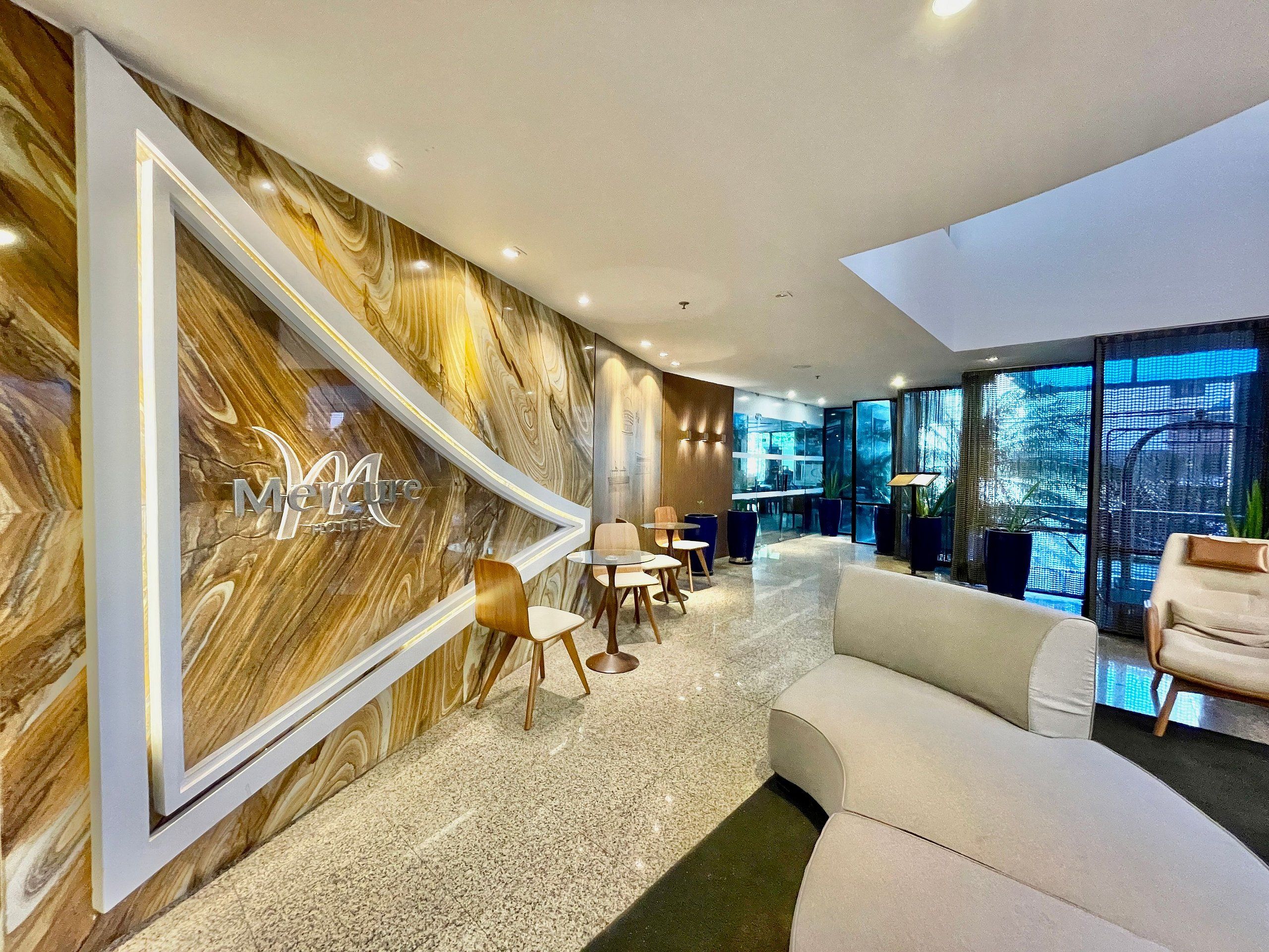Een moderne hotellobby met een marmeren wand, een zithoek en grote ramen.