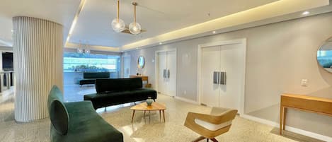 Um lobby moderno com um sofá, uma poltrona, uma mesa de centro e um espelho.