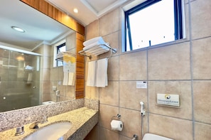 A modern bathroom with a granite countertop sink, a glass shower enclosure, and a towel rack.
