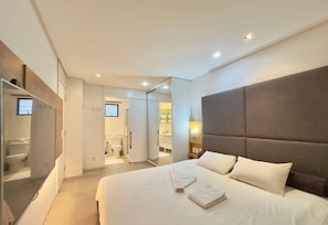 A hotel room with a large bed, a mirror, a wardrobe, and a bathroom visible through an open door.