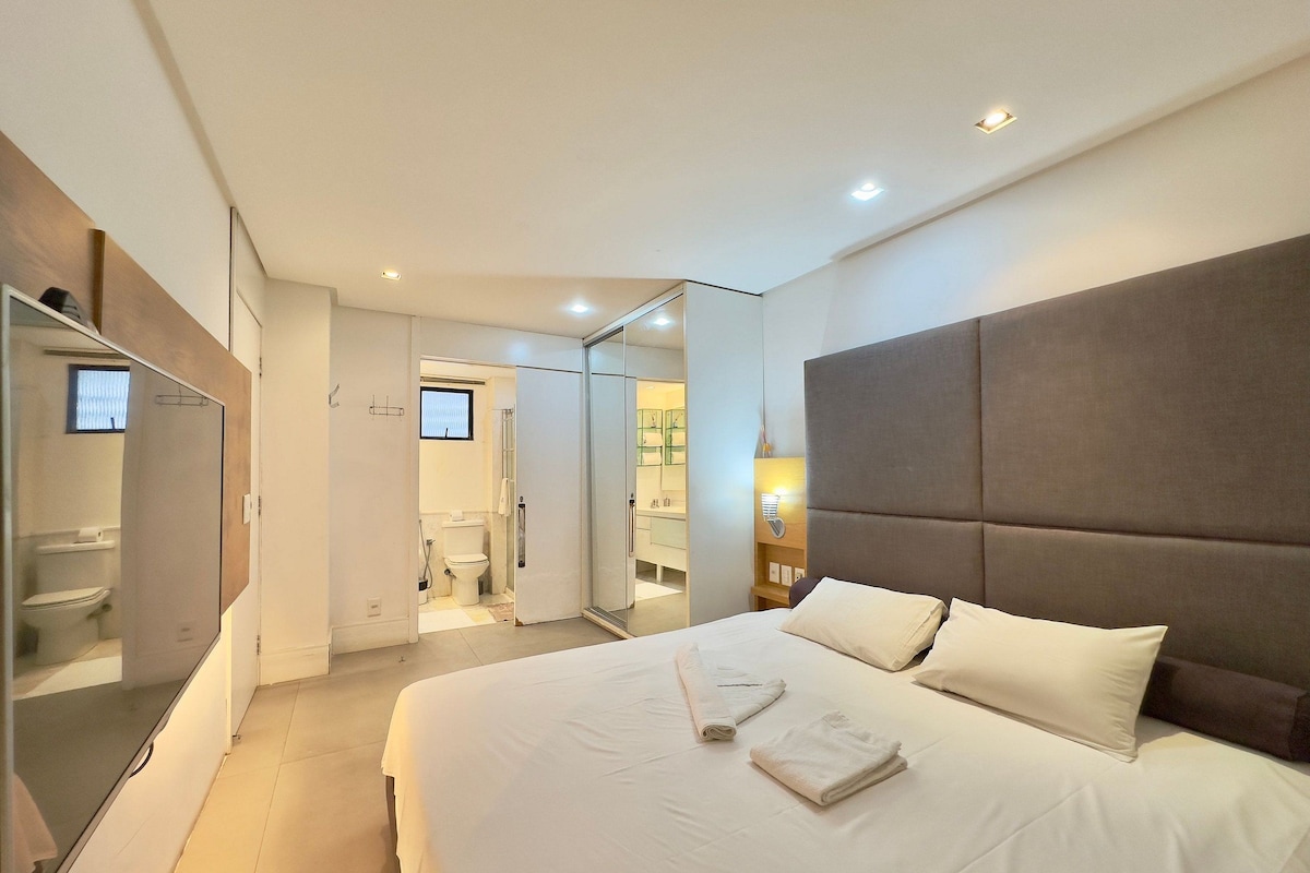 A hotel room with a large bed, a mirror, a wardrobe, and a bathroom visible through an open door.