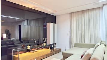 Una sala de estar moderna con una mesa de centro de vidrio, un sofá, un televisor y un espejo grande.