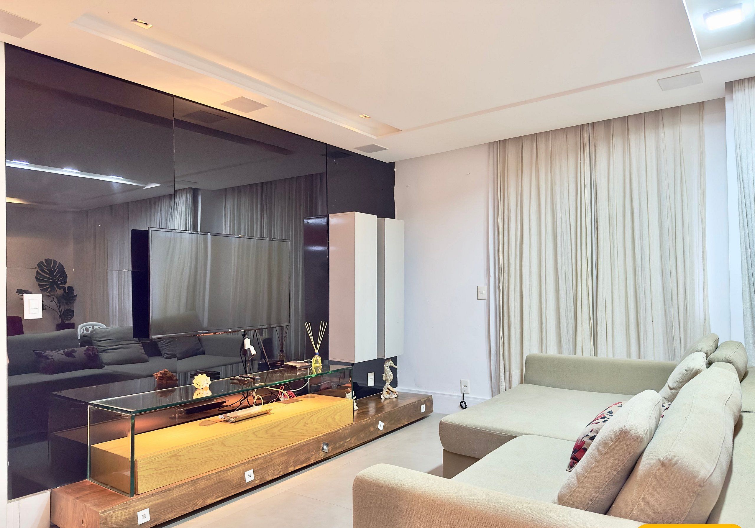 Een moderne woonkamer met een glazen salontafel, een bank, een televisie en een grote spiegel.