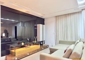 Una sala de estar moderna con una mesa de centro de vidrio, un sofá, un televisor y un espejo grande.