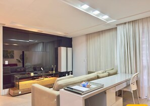 A modern living room with a sofa, a glass coffee table, a dining table, and a chair.
