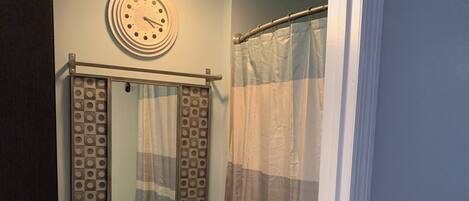 A bathroom with a toilet, a shower curtain, a clock, and a trash can.