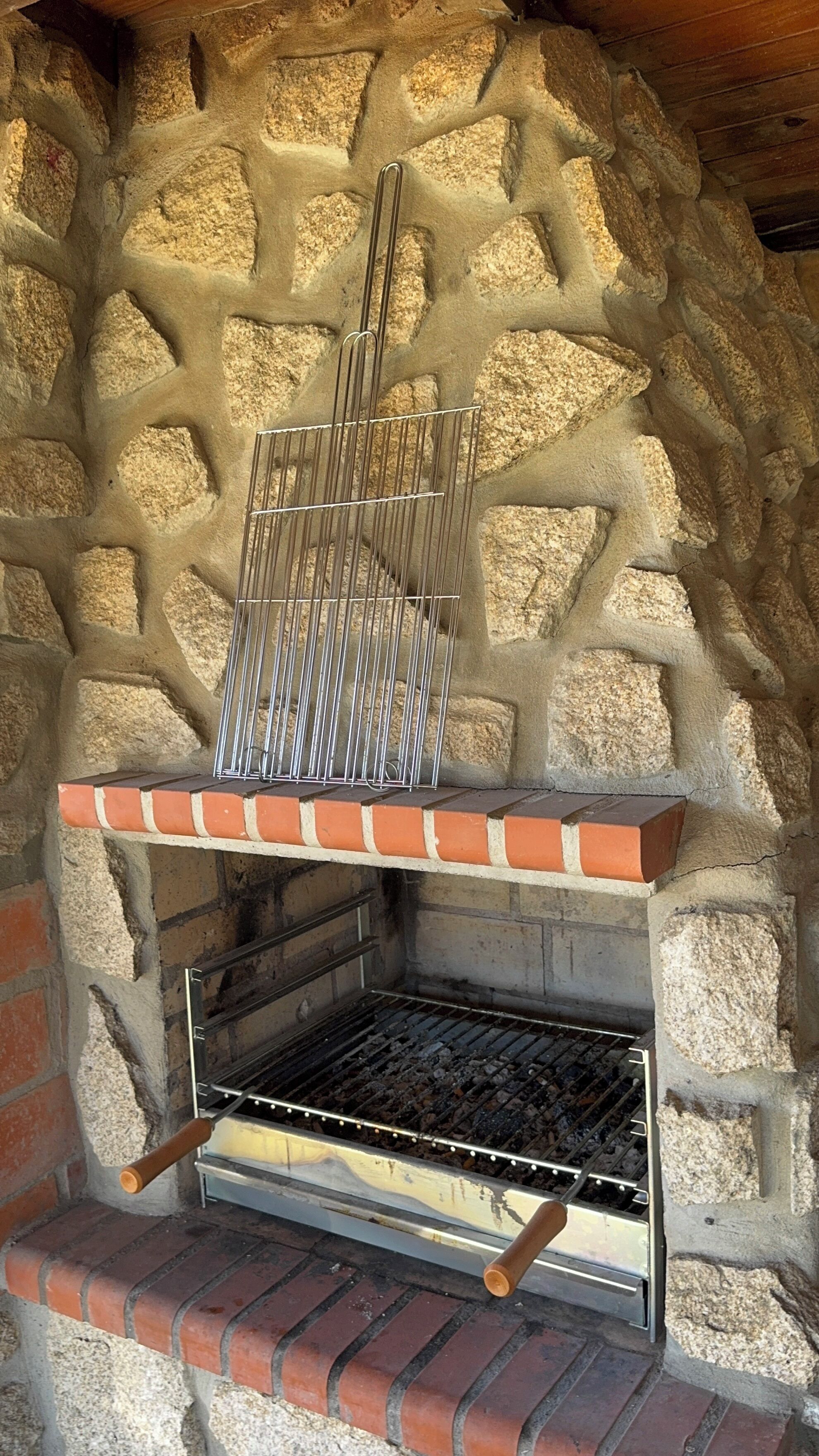 Un four extérieur en pierre, doté d’une grille métallique pour les grillades, d’une base en briques et d’une plaque métallique pour la cuisson.