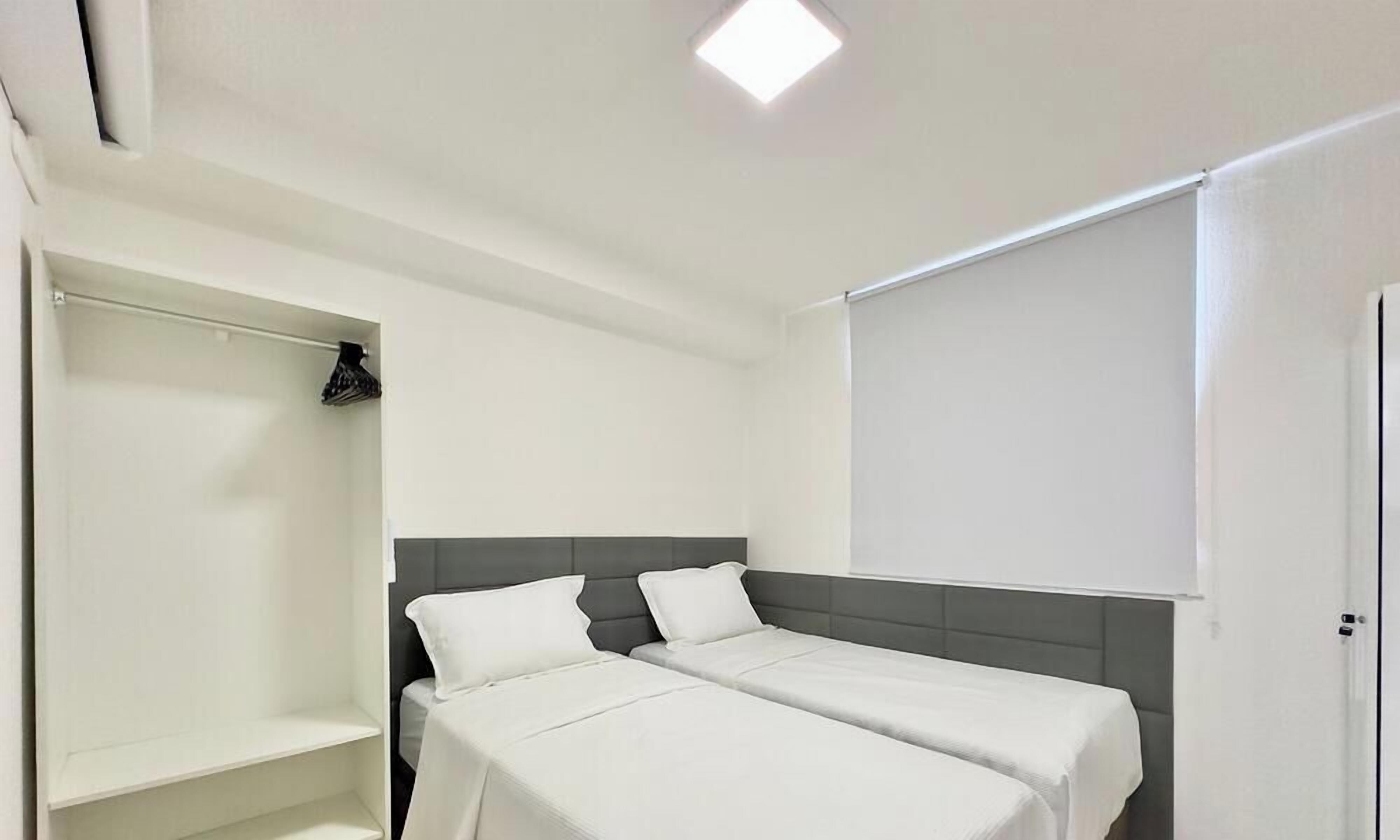 A hotel room with two beds, a wardrobe, and a ceiling light.