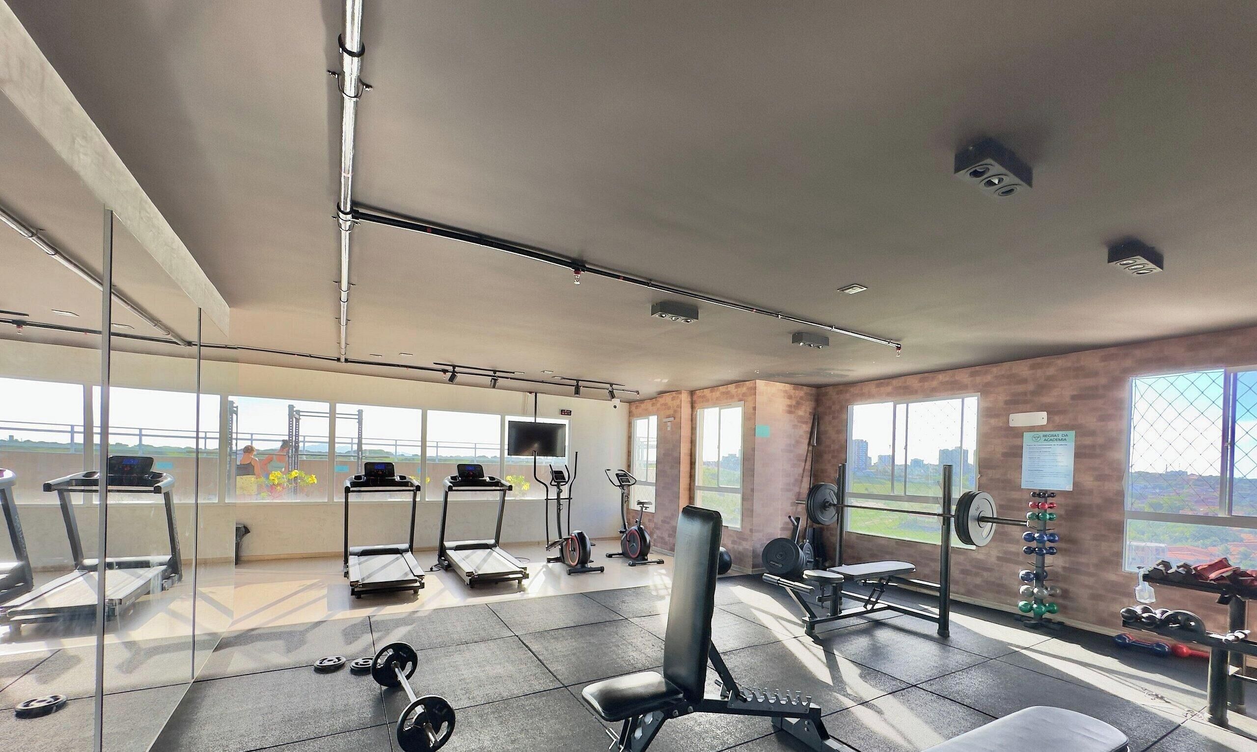 Academia com esteiras, aparelhos de musculação e vista para a cidade.