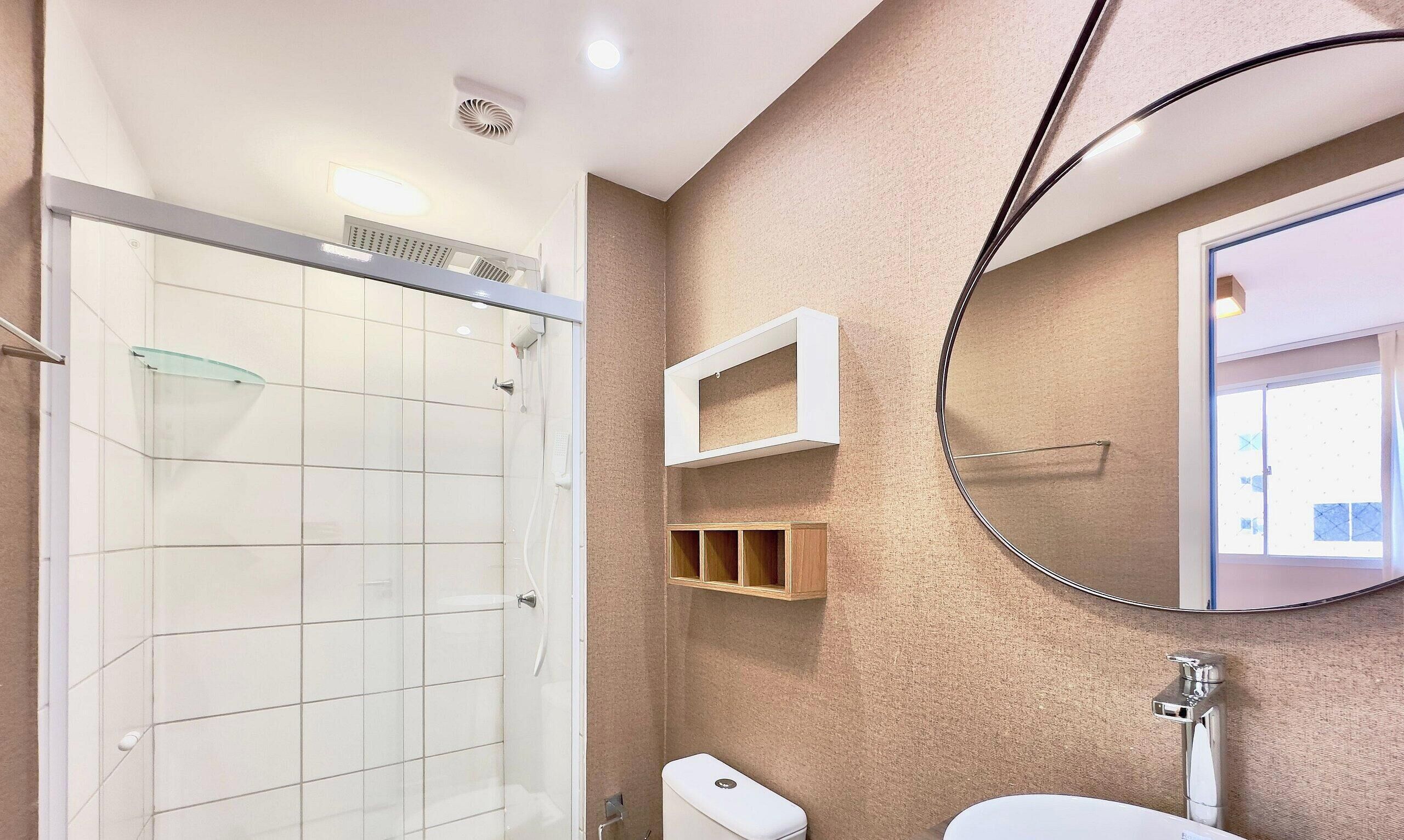 Een badkamer met een douchecabine van glas, een toilet, een wastafel, een spiegel en een plank met een handdoekhouder.