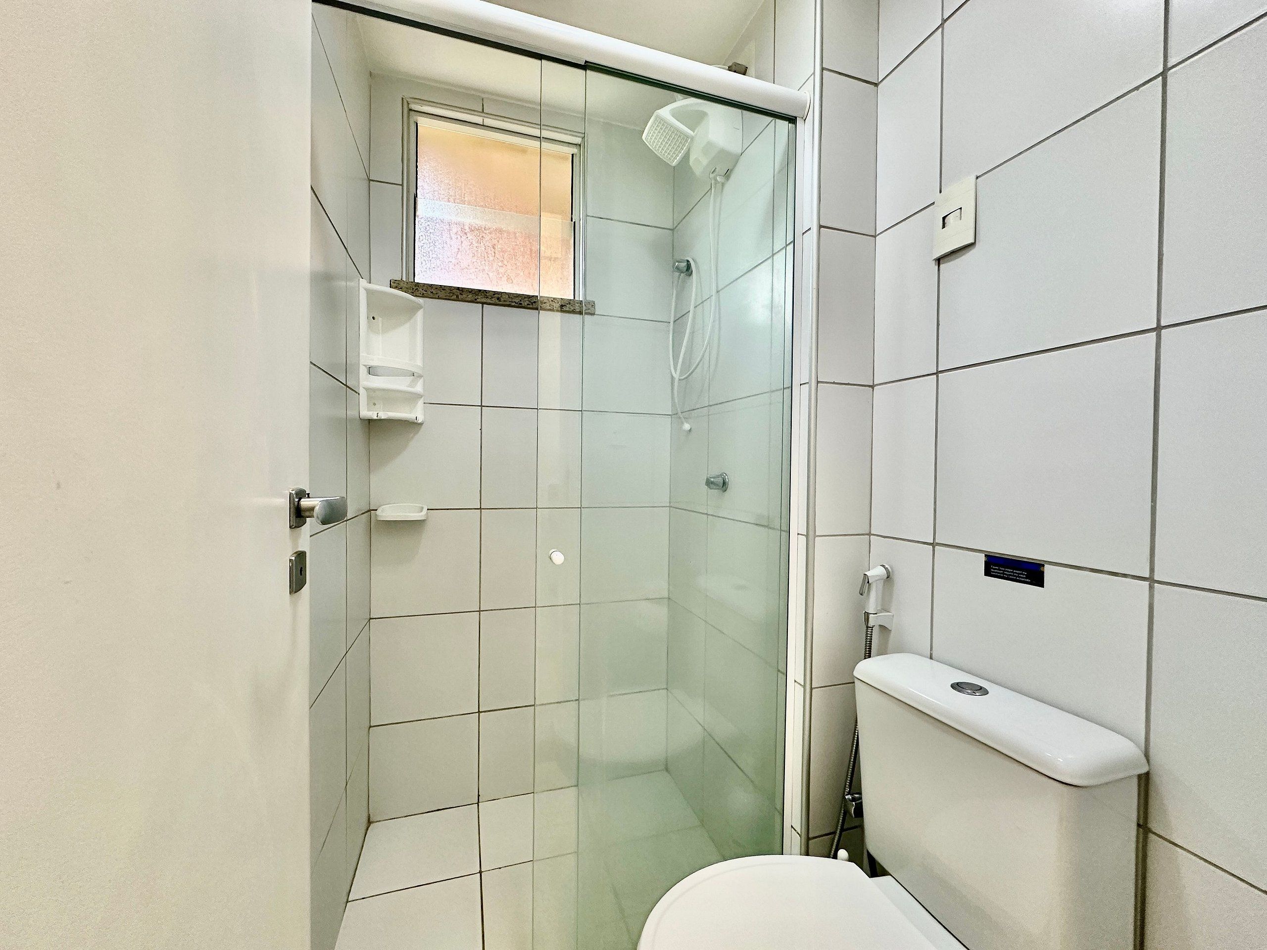 A bathroom with a glass shower enclosure, a toilet, and a small window.