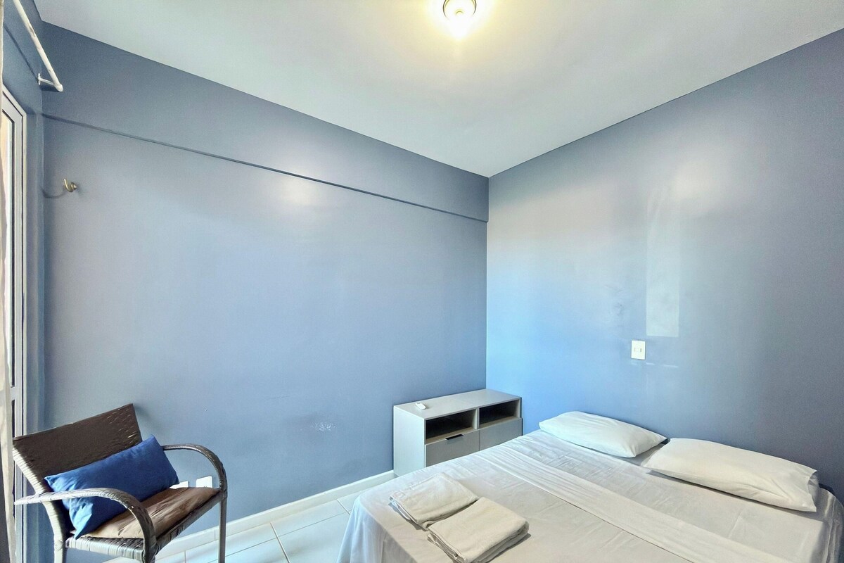 A room with a bed, a chair, a small desk, and a light fixture.