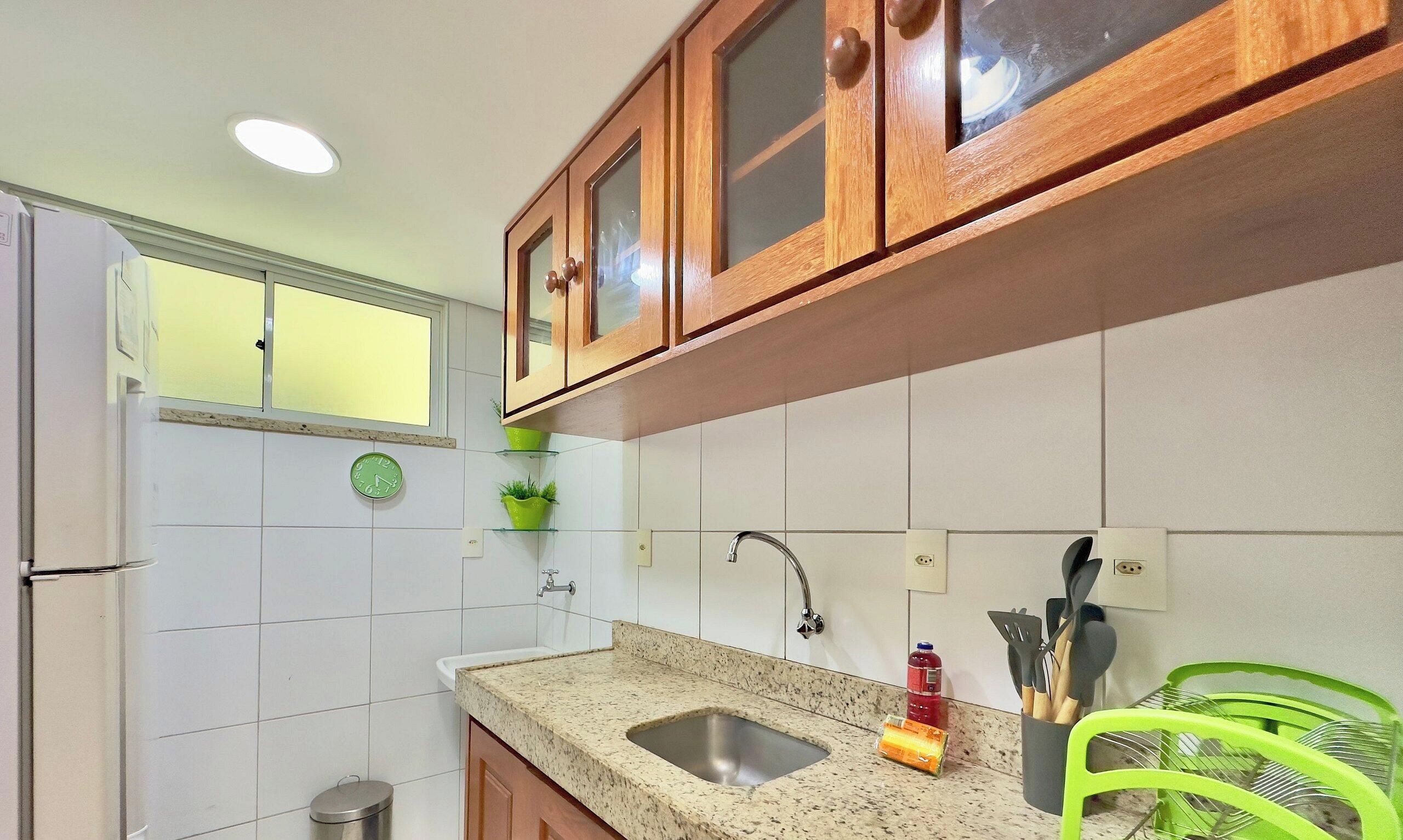 Una cocina con armarios de madera, un lavamanos de acero inoxidable, una planta verde y utensilios de cocina.