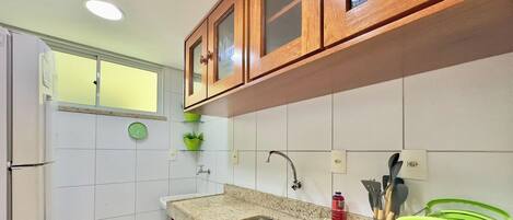 Una cocina con armarios de madera, un lavamanos de acero inoxidable, una planta verde y utensilios de cocina.