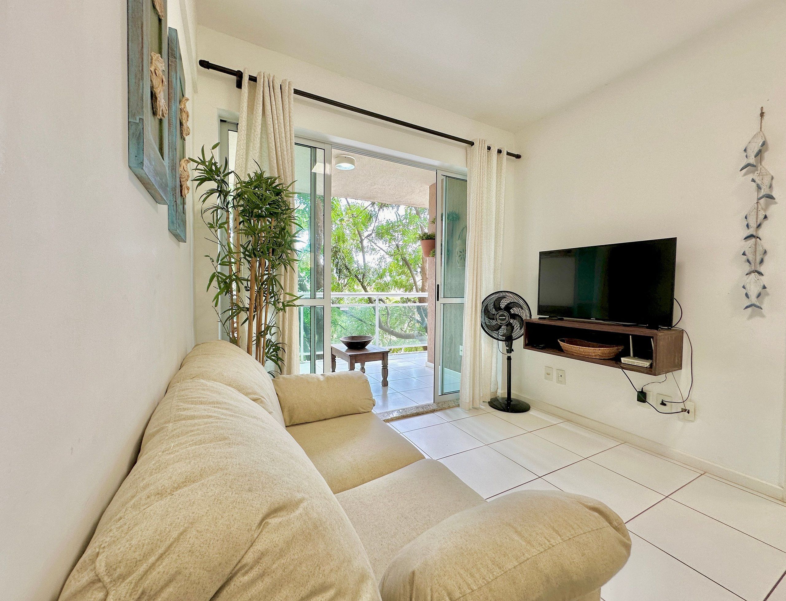 A living room with a sofa, a TV, a fan, and a view of the outdoors.