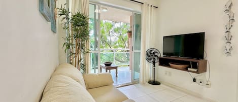 A living room with a sofa, a TV, a fan, and a view of the outdoors.