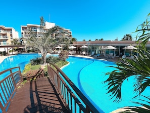 A swimming pool with a wooden deck, lounge chairs, and umbrellas. - Palm Beach Porto das Dunas - CE (Aquiraz)