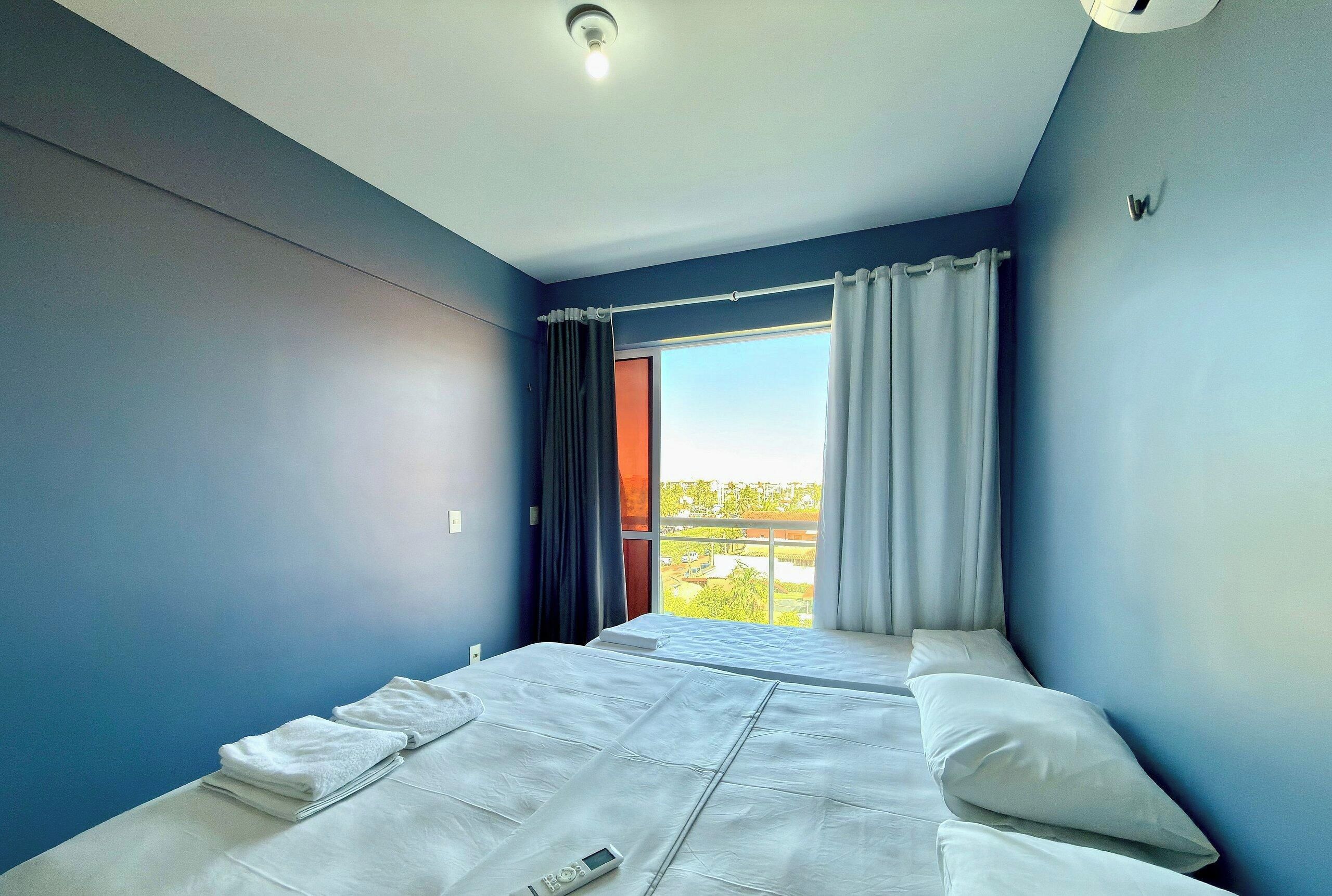 A room with a bed, a window with curtains, and a view of the outside.